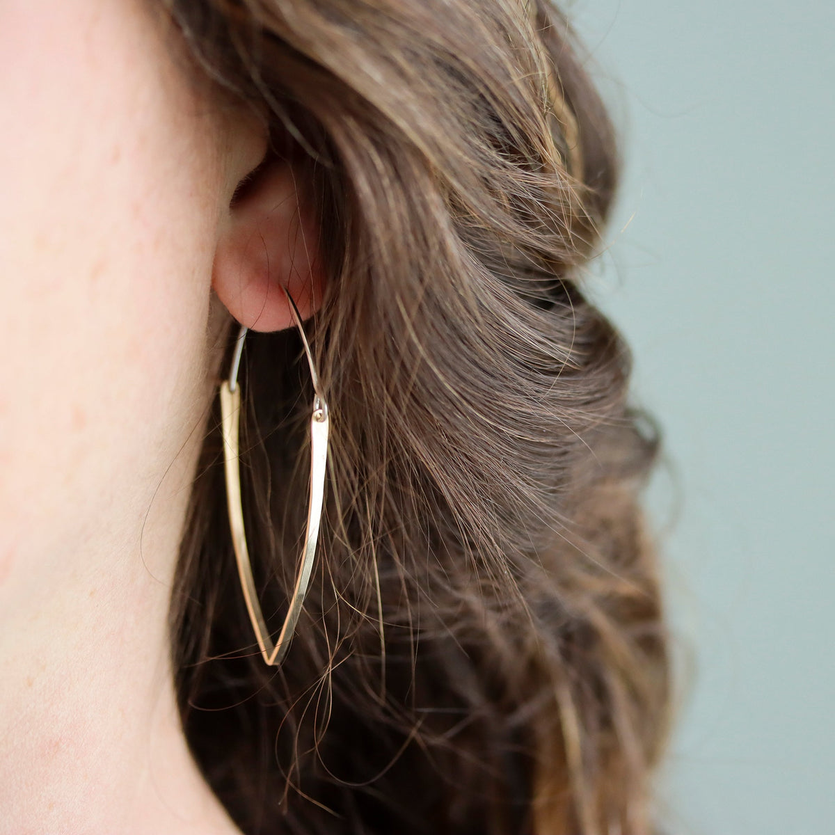 Gold hoop earrings worn by a person with wavy hair against a light blue background