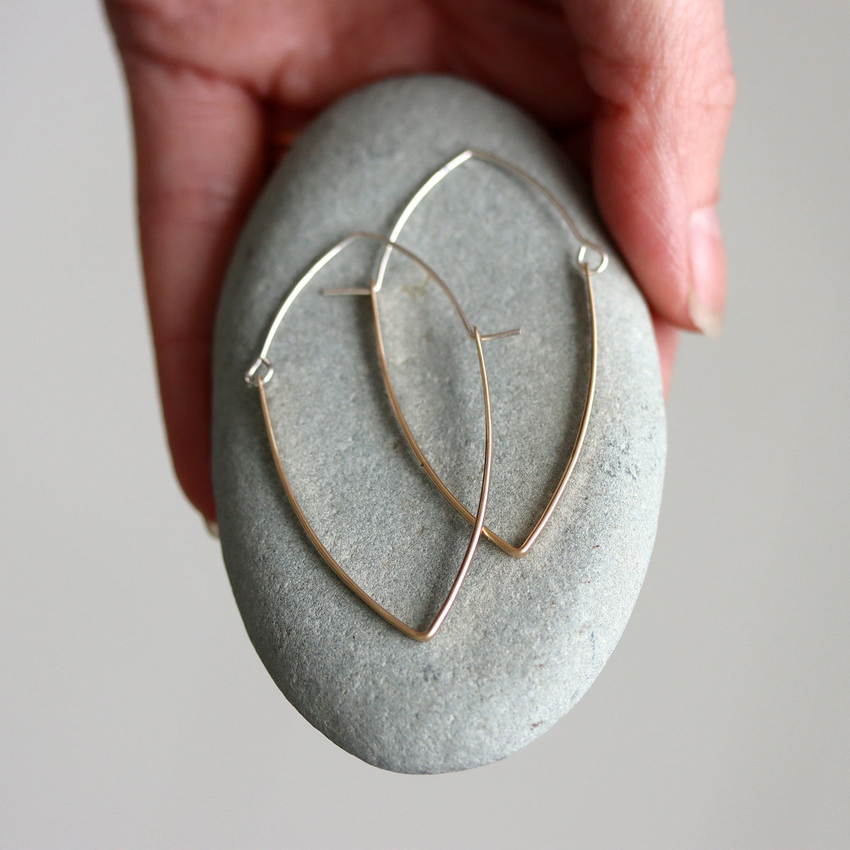 Gold hoop earrings on a gray stone with a hand holding it from above
