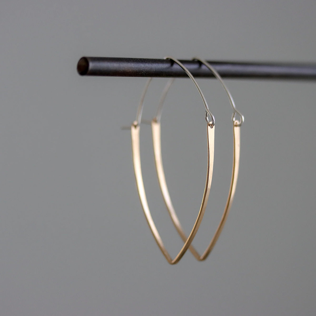 Gold hoop earrings hanging on a black rod against a gray background