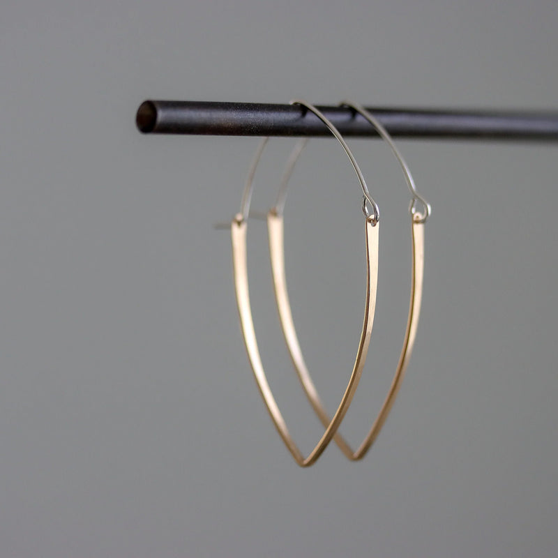 Gold hoop earrings hanging on a black rod against a gray background