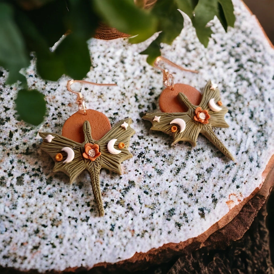 Pair of earrings with leaf and moon design on a textured surface