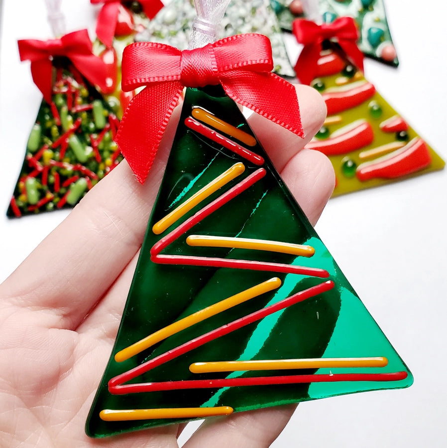 Hand holding a green Christmas tree-shaped ornament with red and yellow sticks, surrounded by similar ornaments.