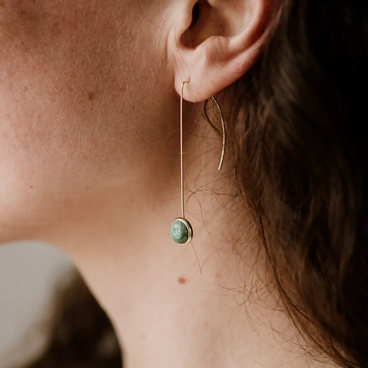 Close-up of an ear wearing a green gemstone earring with a blurred background
