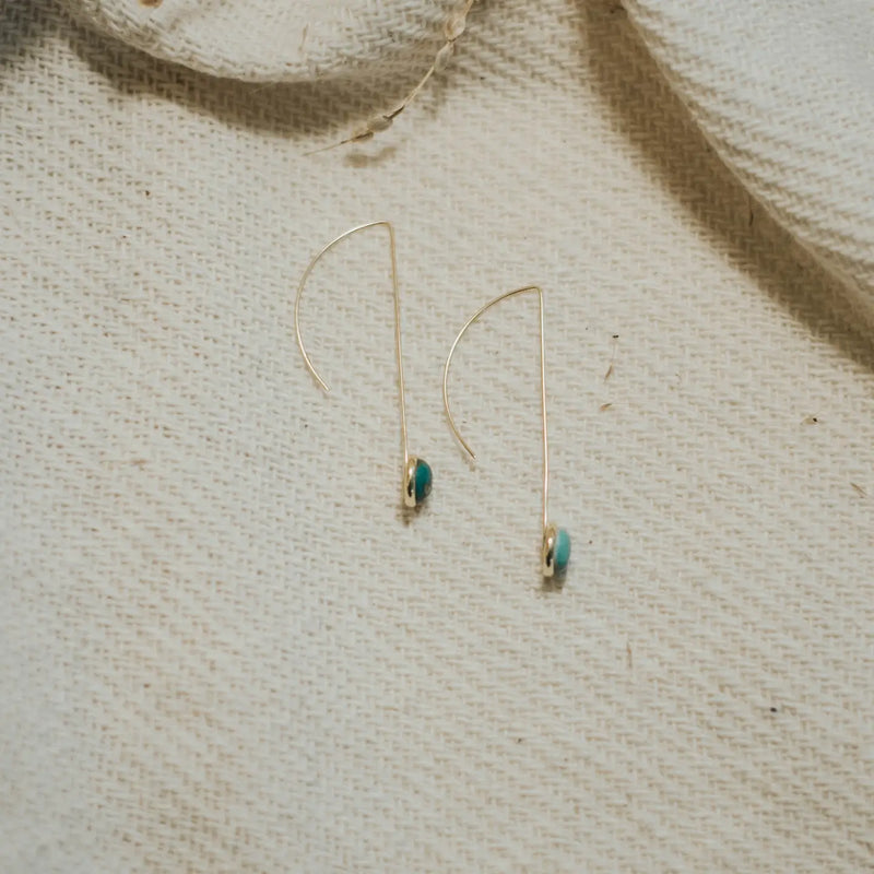 Gold earrings with turquoise stones on a textured beige fabric background