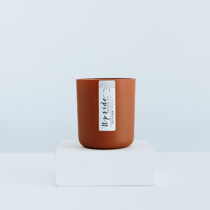 A brown coconut soy candle in a cylindrical jar with a white label that reads 'Upside Goods Co. Autumn Grove Limited Edition.