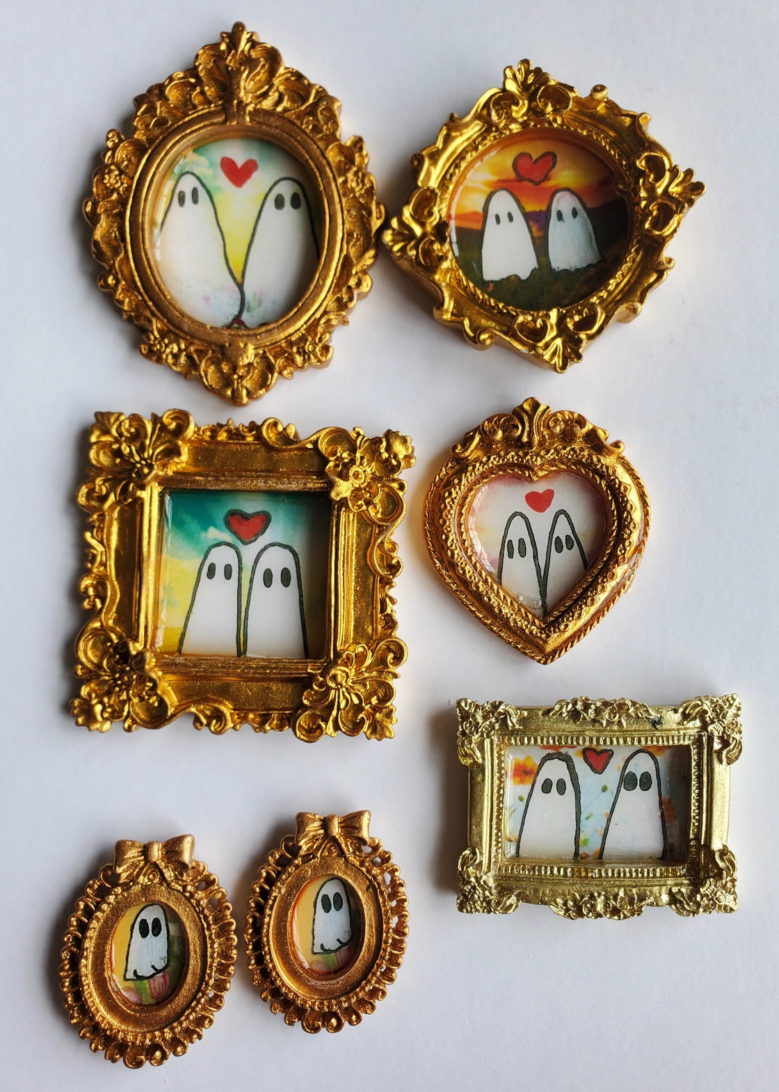 Set of small gold-framed pictures with cartoon ghosts and hearts on a white background