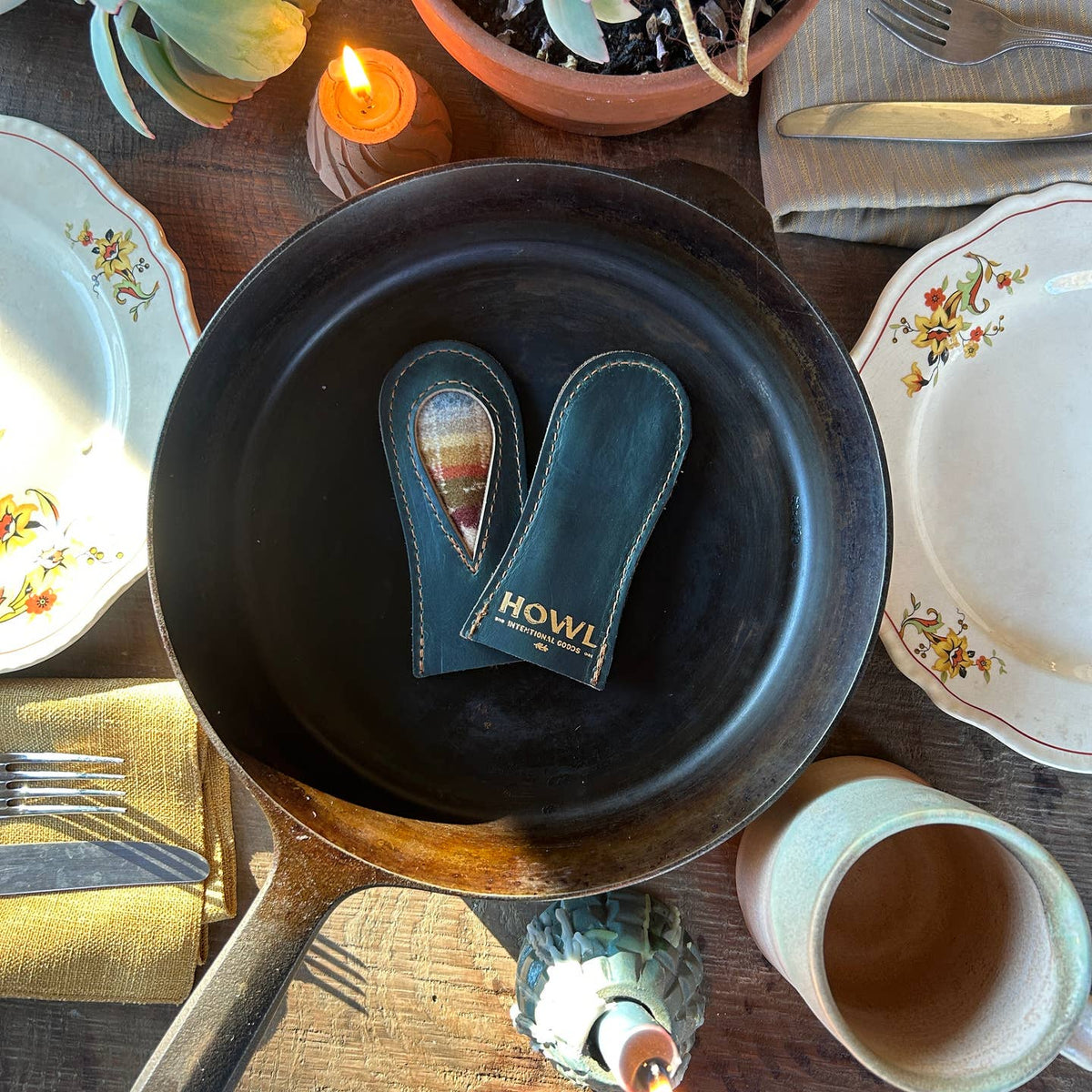 Two leather hot pads with 'HOWL' branding on a black frying pan on a rustic table setting.