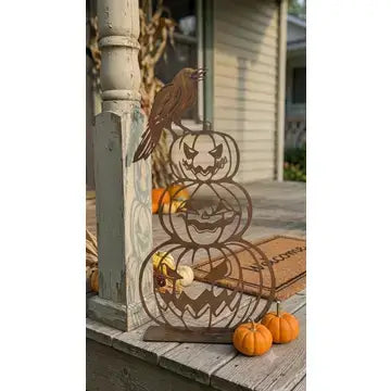 A decorative metal Halloween gate with a stacked jack-o'-lantern design and a crow perched on top, displayed on a wooden porch with small pumpkins and a house in the background.