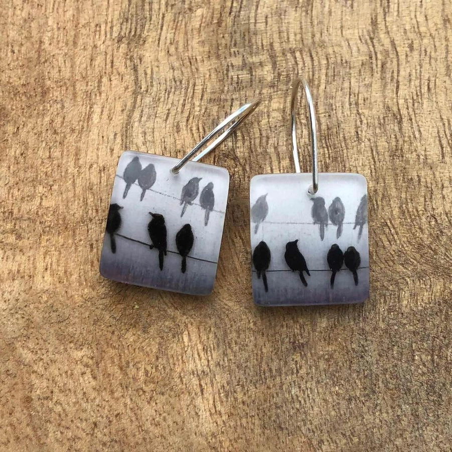 Square earrings with bird design on a wooden surface