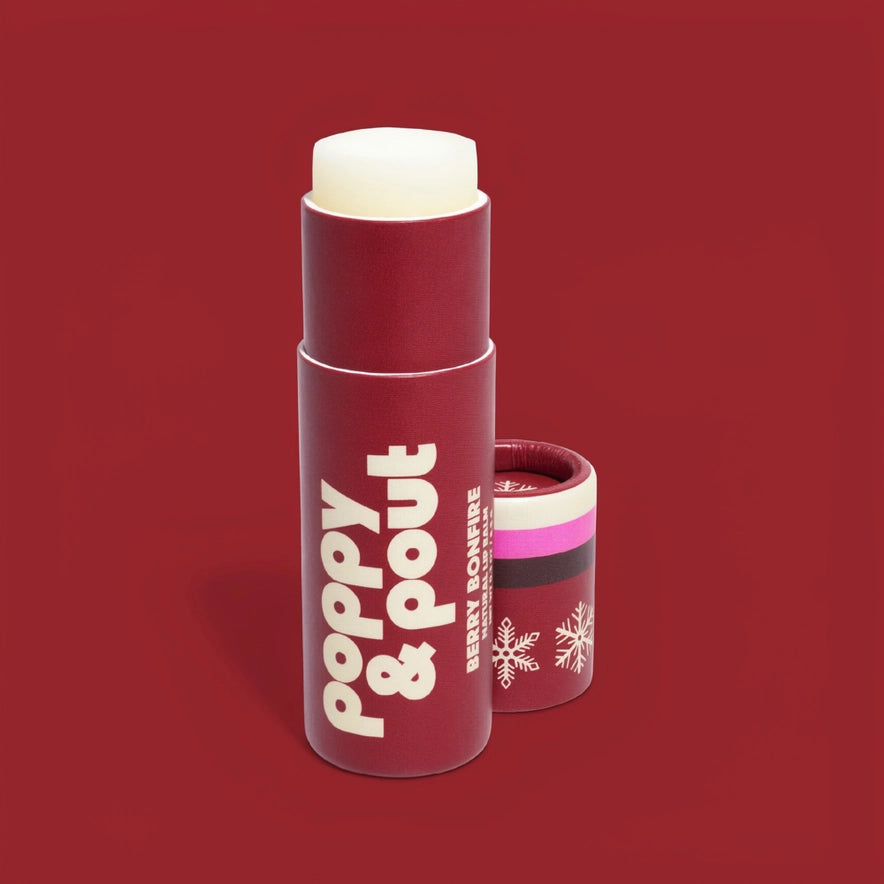 A red cosmetic stick container labeled 'poppy & pout' with a white lip balm visible at the top, shown on a solid red background with the cap placed beside it.