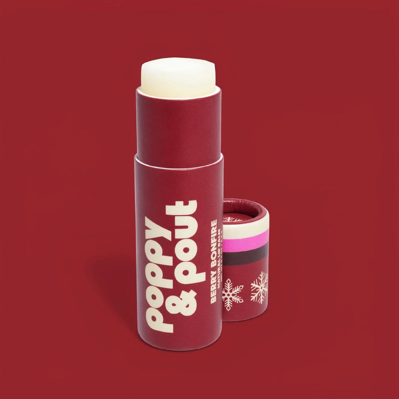 A red cosmetic stick container labeled 'poppy & pout' with a white lip balm visible at the top, shown on a solid red background with the cap placed beside it.