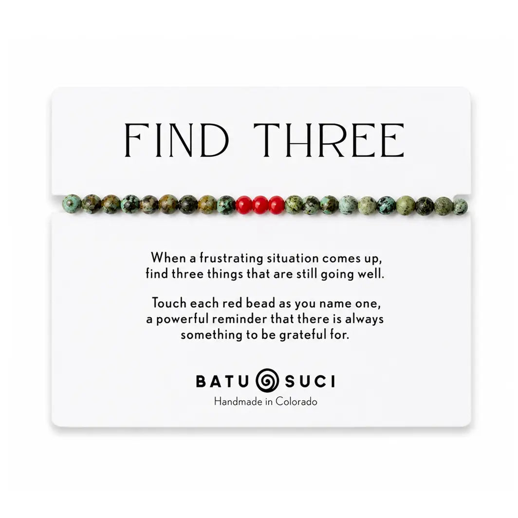 A beaded bracelet with mostly green marbled beads and three red beads, displayed on a white card that reads 'FIND THREE' with a short inspirational message and the brand name Batu Suci.