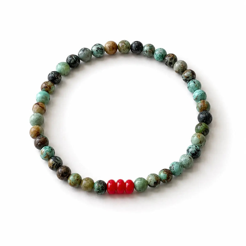 A beaded stretch bracelet featuring natural stone beads in green, brown, and black, accented by three bright red spacer beads, shown on a plain white background.