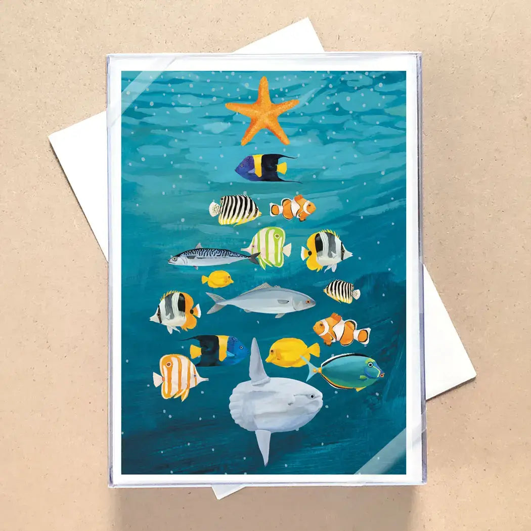A square art print featuring an underwater scene with a starfish, tropical fish, and a large white shark swimming upward through blue water, displayed on a beige surface with a white envelope behind it.