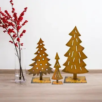 Three rust-colored metal Christmas tree ornaments of different sizes displayed on a light wood floor next to a glass vase with red berries.