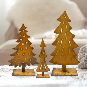 Three rusted metal Christmas tree cutout ornaments in different sizes, displayed on a white textured surface with a soft, blurred background.