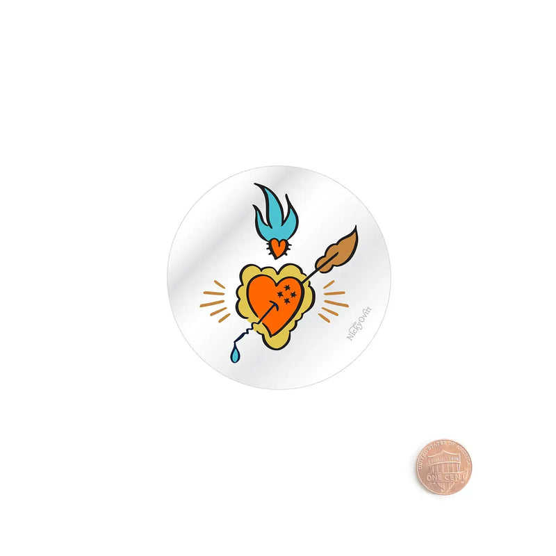 A round white sticker or button featuring a colorful Holy Trinity design with a burning heart pierced by an arrow, shown on a white background with a penny for scale.