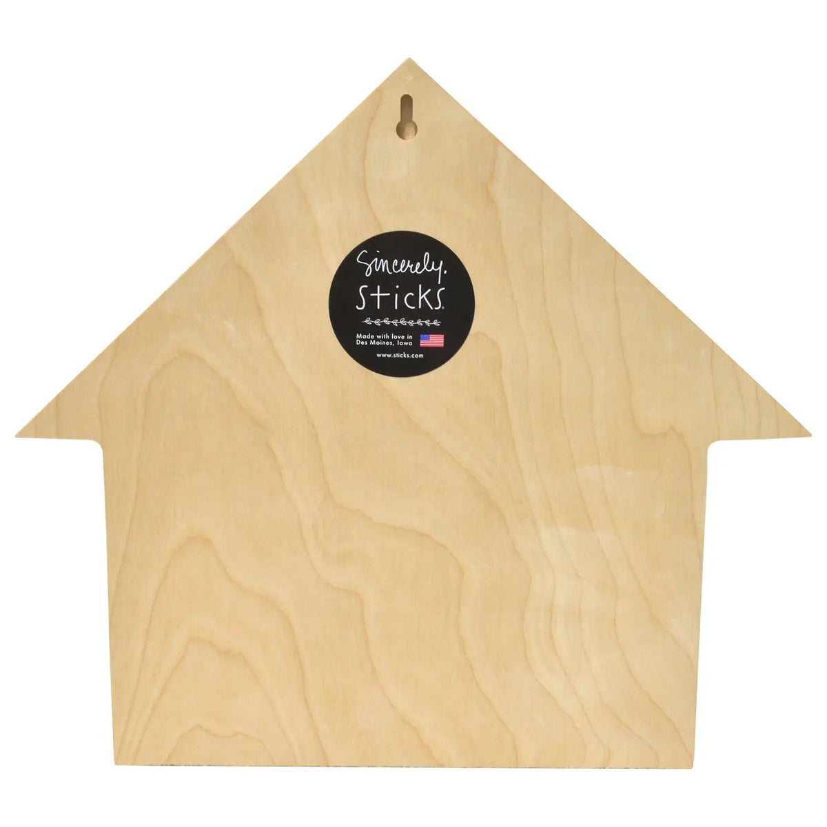 A house-shaped wooden board with a natural light wood grain finish, featuring a small hanging hole at the top and a black circular 'Somewhat Sticks' brand label in the center, set against a plain white background.