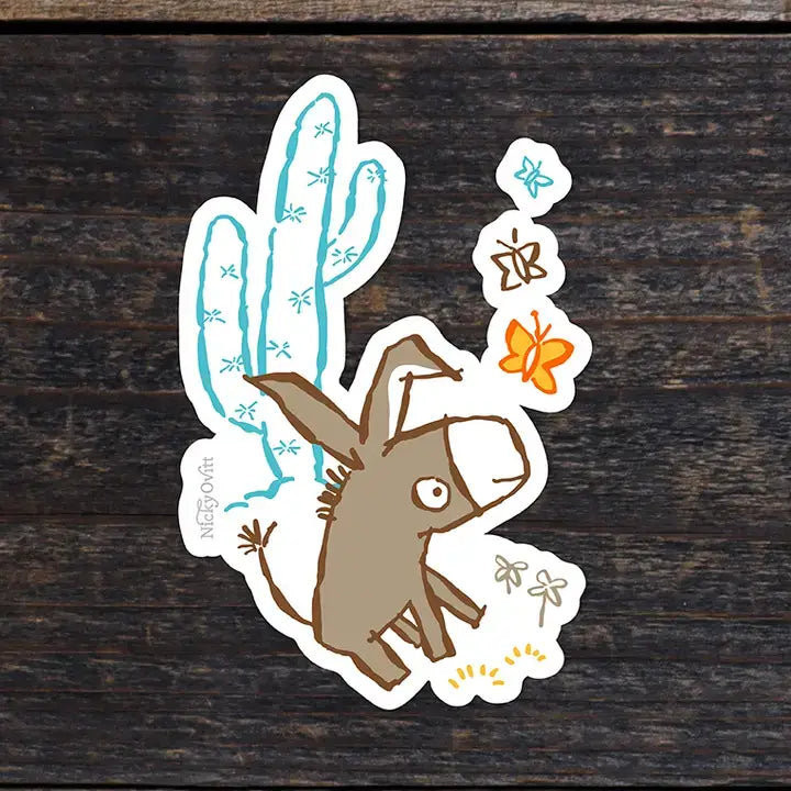 A die-cut sticker featuring a cartoon donkey with a blue cactus and orange butterfly design, placed on a dark wood background.