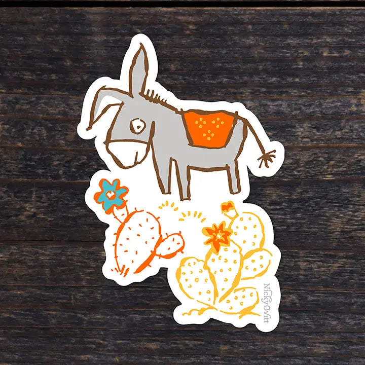 A die-cut sticker featuring a hand-drawn donkey with an orange saddle blanket, orange cactus, yellow cactus, and small flowers, placed on a dark wood background.