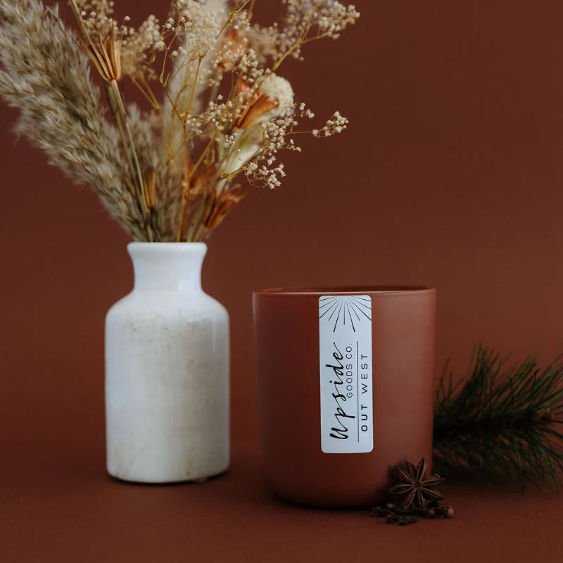 Ceramic vase with dried flowers and a brown candle labeled 'Upside Goods Co' on a brown background
