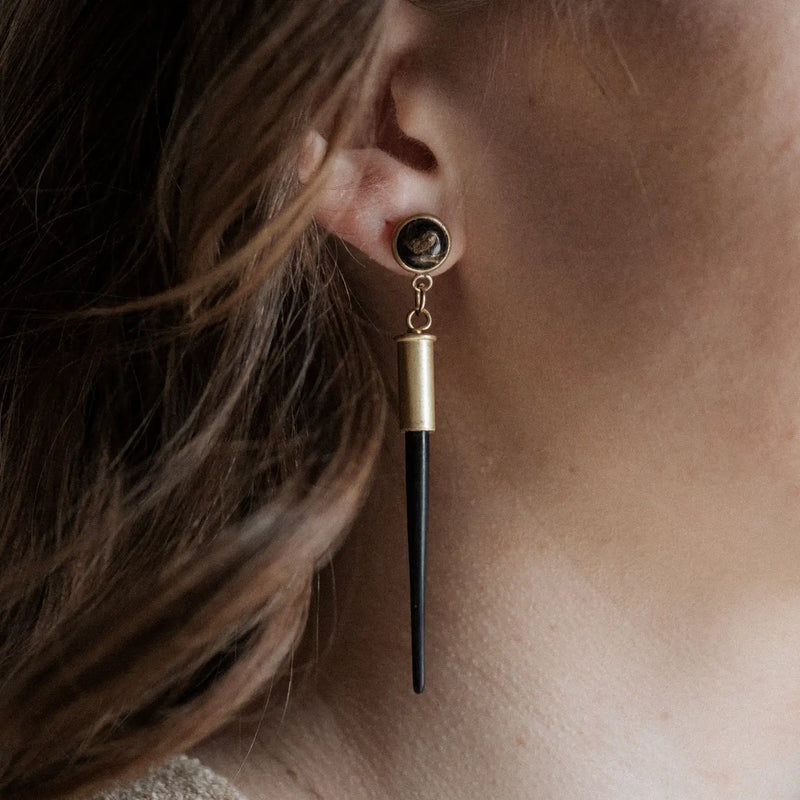Close-up of an earring with a porcupine, obsidian, and gold design on a person's ear.