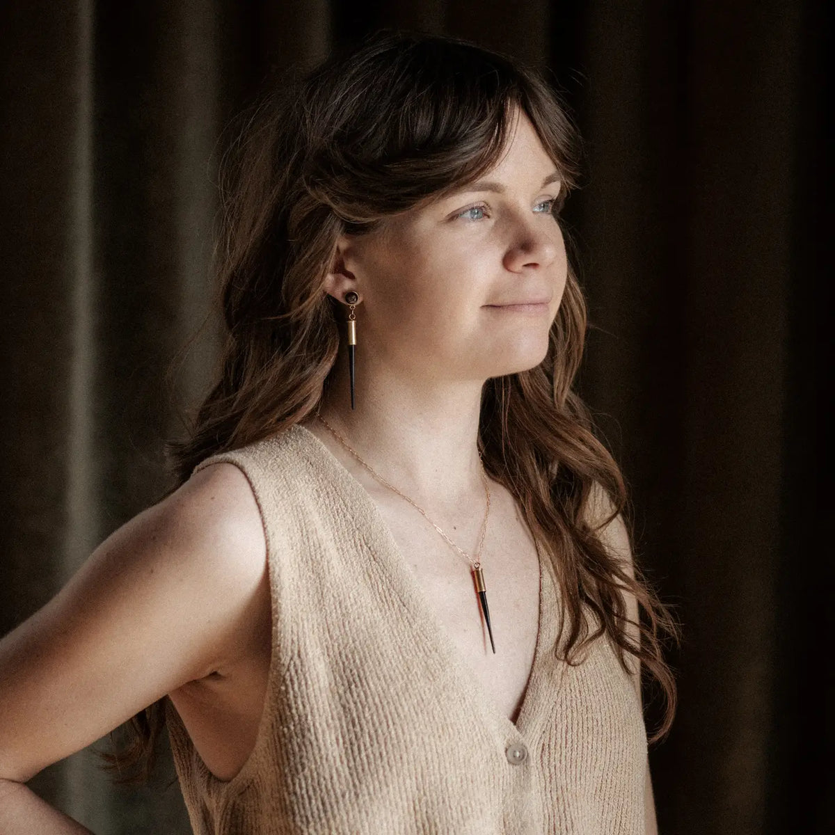 Woman wearing a beige sleeveless top with a dark background wearing COmmonform earrings