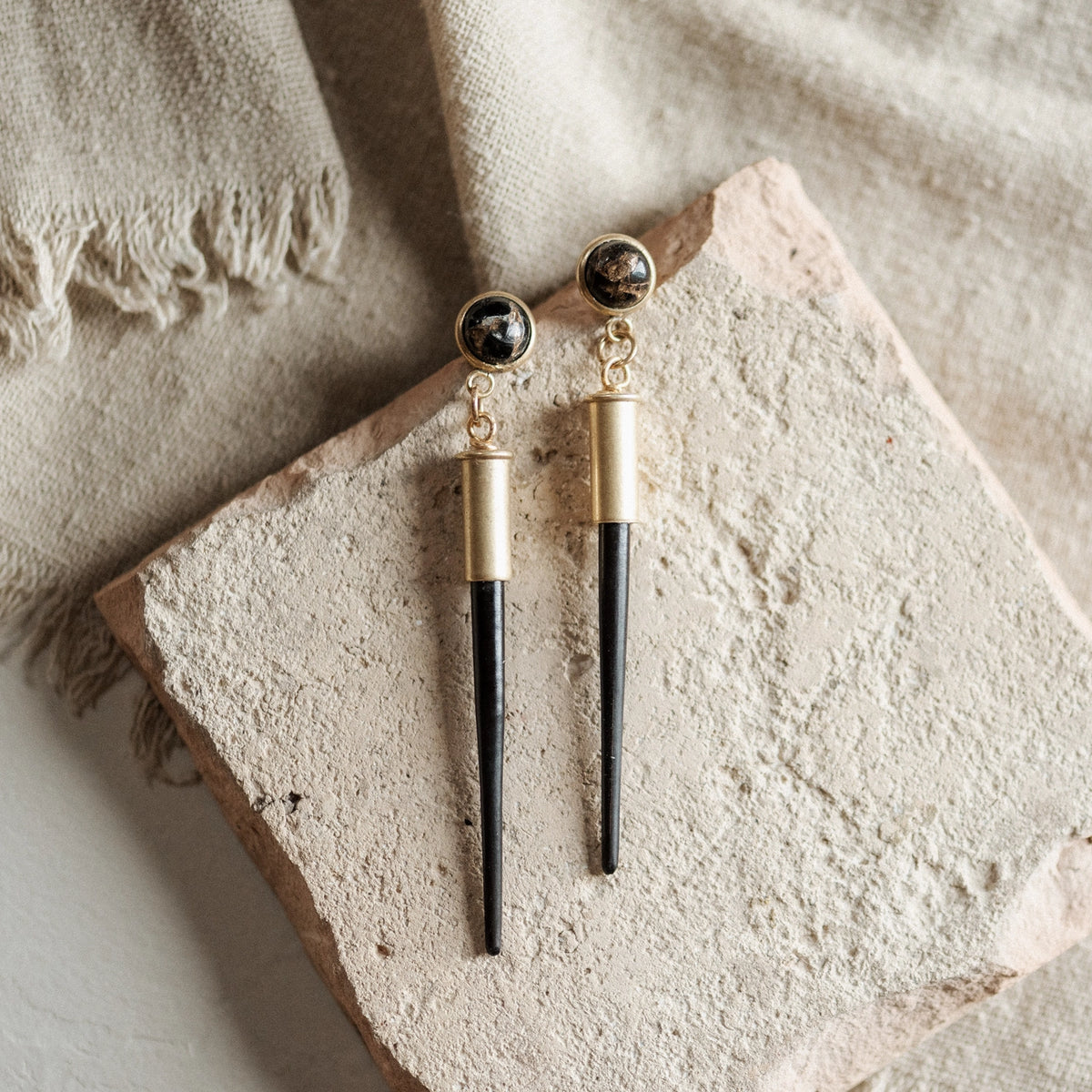 Pair of earrings with gold and black  porcupine quill and bullet casing components on a textured stone surface