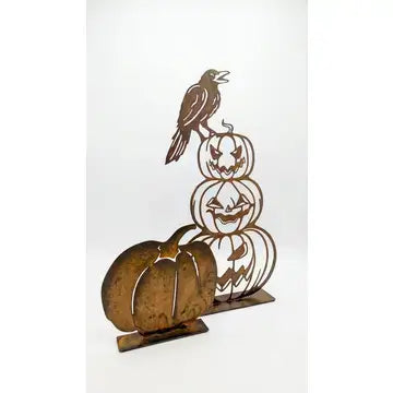 Rustic metal Halloween decoration featuring a crow perched atop a stacked trio of carved jack-o'-lantern pumpkins, displayed on a plain white background.
