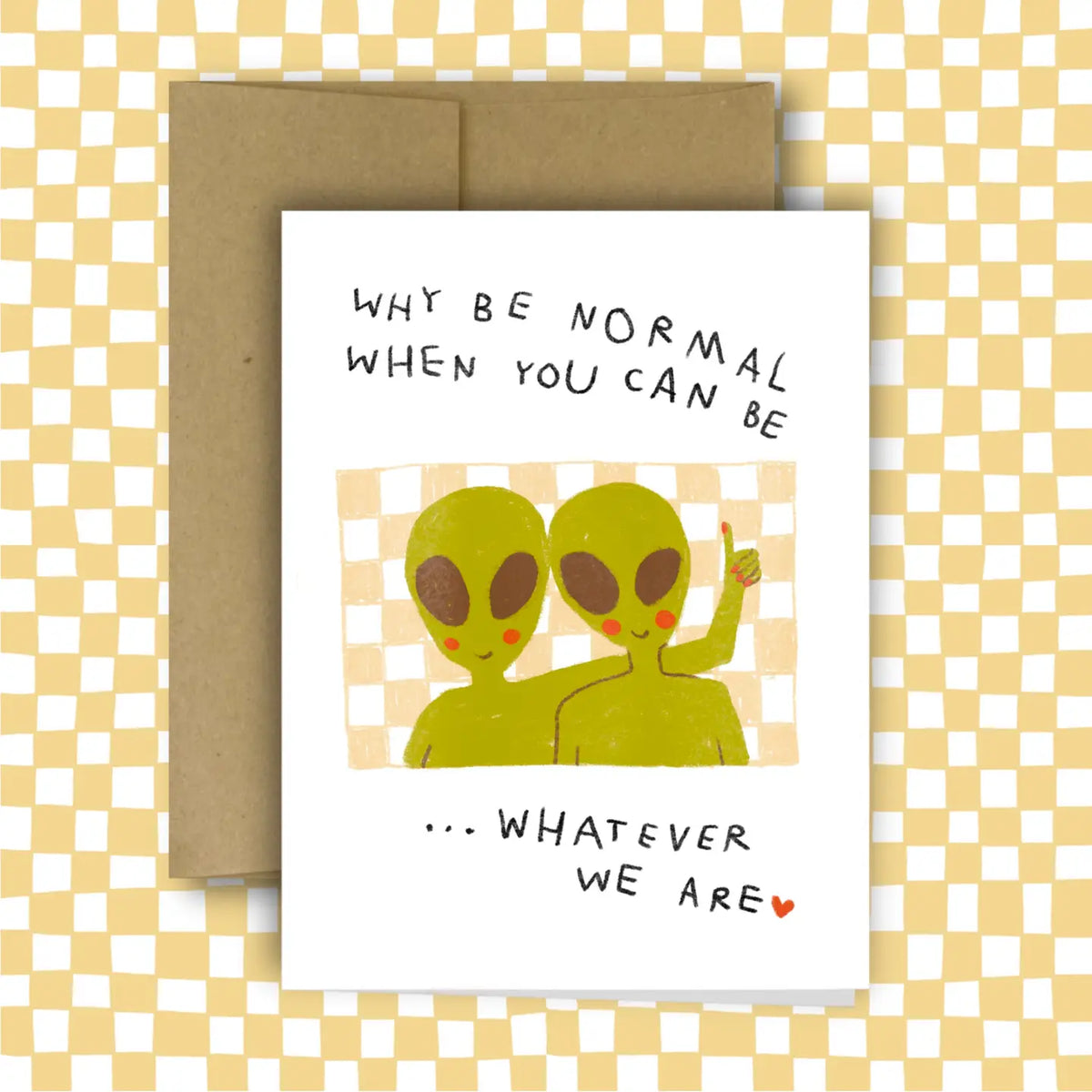 A white greeting card with a brown envelope behind it, featuring an illustration of two green aliens and the text 'WHY BE NORMAL WHEN YOU CAN BE .