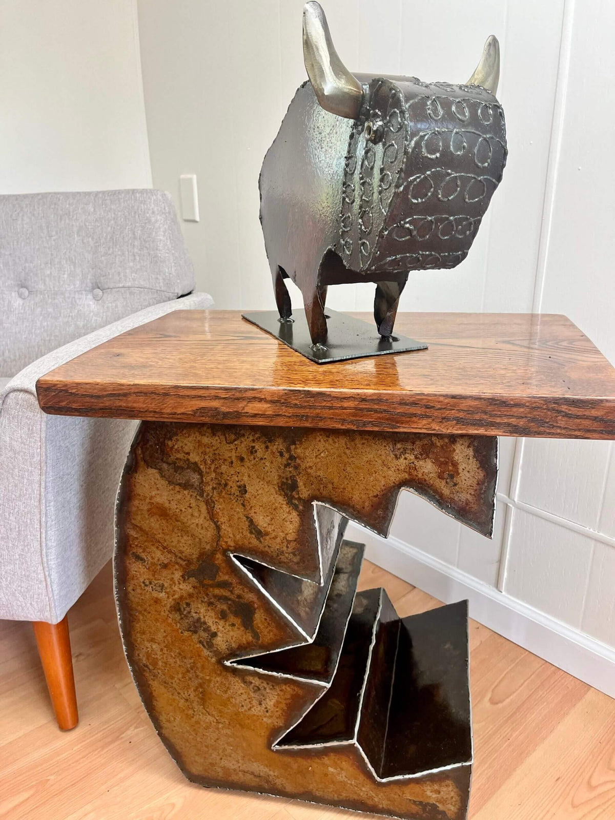 A rustic metal biosn sculpture displayed on a wooden and sculptural side table in a living room setting.