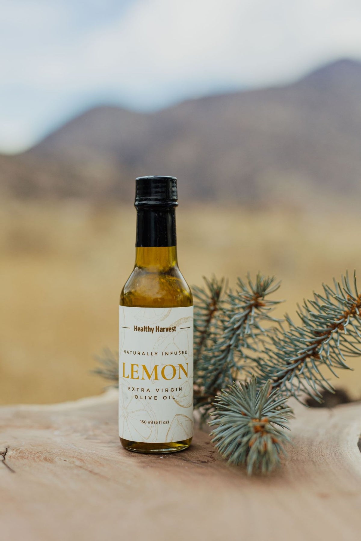 Lemon Infused Olive Oil photographed with a sprig of pine and out of focus mountain landscape in background