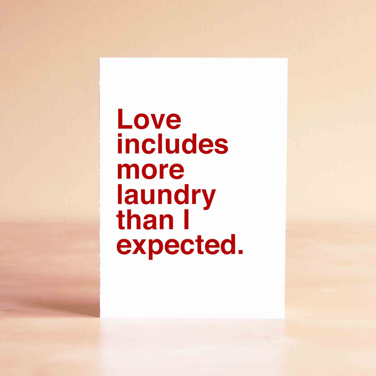 White card with red lettering reading "Love includes more laundry than I expected."