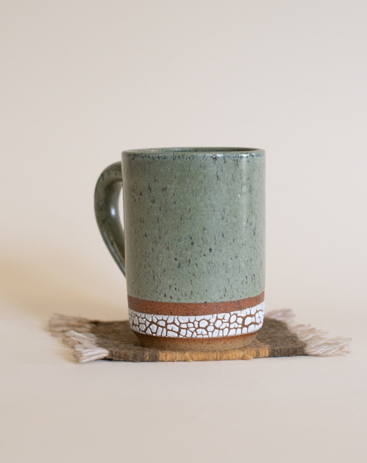 Green Tea Colored + Crawl Glaze on Speckled Buff Ceramic Mug displayed on a coaster rug