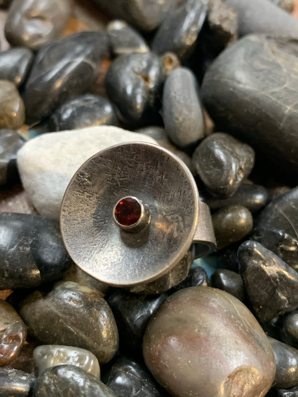 black river rock background for a sterling silver concave disk ring with a garnet in the center